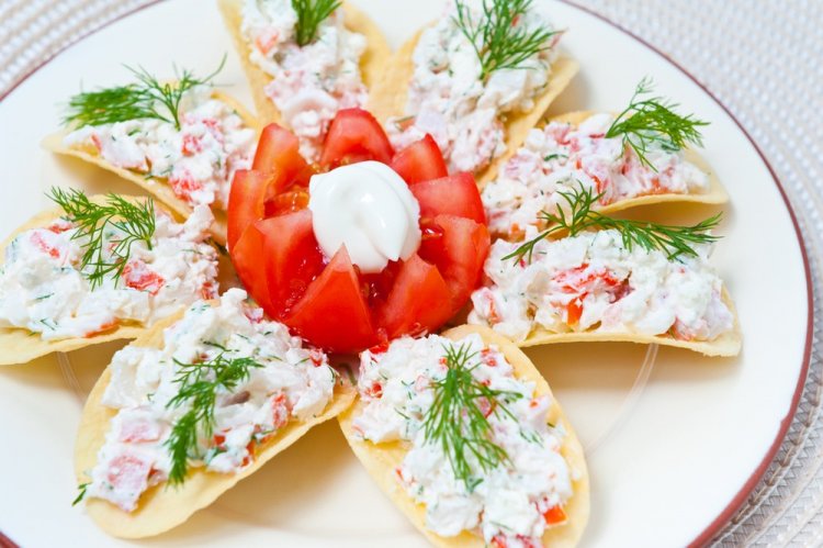 Aperitivo con tomates y palitos de cangrejo sobre patatas fritas